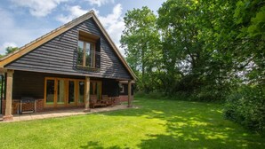 A house with a sloped roof, a covered porch with chairs, and a grassy yard. - 4 Bed in Fakenham (oc-1261) (Thursford)