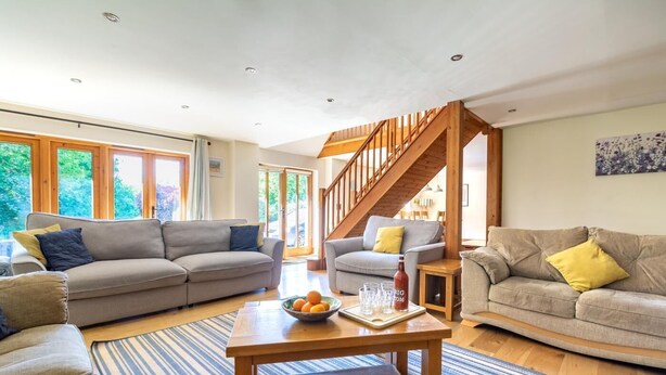 A spacious living room with two sofas, a coffee table, and a wooden staircase. - 4 Bed in Fakenham (oc-1261) (Thursford)