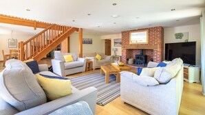 A spacious living room with a staircase, a fireplace, and a television. - 4 Bed in Fakenham (oc-1261) (Thursford)