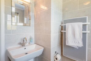 A bathroom with a sink, mirror, towel rack, and toilet paper holder.