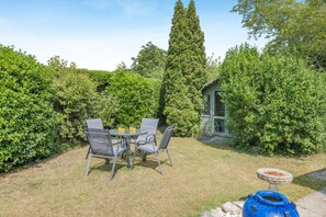 A patio with a table and chairs, surrounded by dense greenery and a tall tree. - 2 Bed in Langham (oc-1539) (Langham)