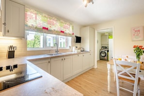 A modern kitchen with a large window, built-in appliances, and a dining area with a table and chairs. - 2 Bed in Langham (oc-1539) (Langham)