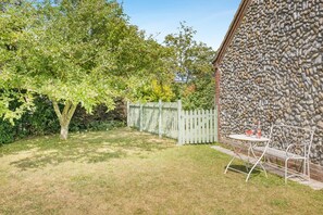 A backyard with a stone wall, a wooden fence, and a metal table and chair set. - 2 Bed in Langham (oc-1539) (Langham)