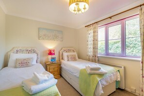 A bedroom with two beds, a nightstand with a lamp, a painting on the wall, and a window with curtains.