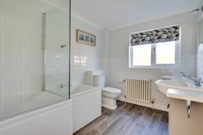 A bathroom with a glass shower enclosure, a white bathtub, a toilet, a sink, and a window with a stone wall above it. - 3 Bed in Langham (oc-1369) (Langham)