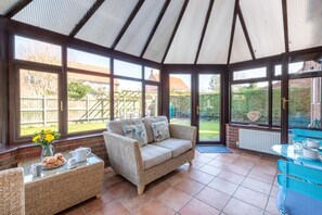 A conservatory with a wicker sofa, a coffee table, and a dining table with chairs. - 3 Bed in Langham (oc-1369) (Langham)