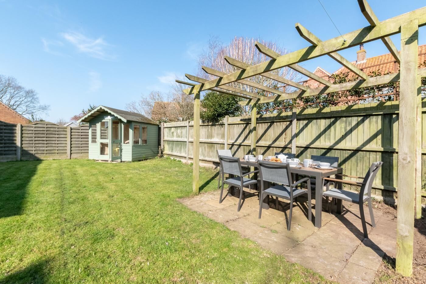A patio area with a table and chairs, a wooden pergola, and a small shed in the background.