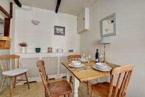 A dining area with a wooden table set for two, chairs, a white cabinet, a framed picture, and a lamp. - 2 Bed in Wells-next-the-sea (oc-1279) (Wells-next-the-Sea)