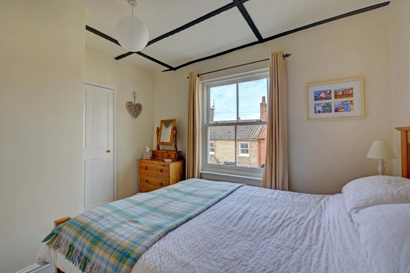 A bedroom with a bed, dresser, window, and a framed picture on the wall.