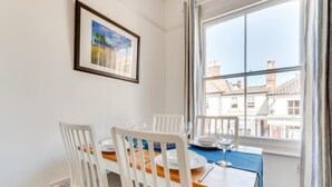 Ein Essbereich mit einem für vier Personen gedeckten Tisch, weißen Stühlen, einer blauen Tischdecke und einem gerahmten Bild an der Wand.