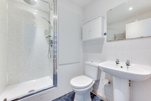 Une salle de bain moderne avec une douche à parois de verre, des toilettes blanches et un lavabo blanc avec un miroir au-dessus.