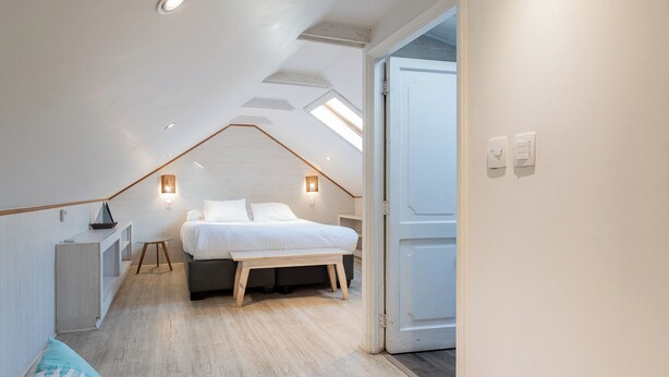 Un dormitorio con cama, mesitas de noche, un banco y un tragaluz.