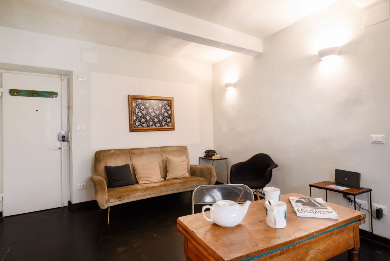 Et værelse med en brun lædersofa, et lille bord med te og kopper, et billede med blomstermotiv på væggen og en bærbar computer på et natbord.