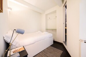 Ein Hotelzimmer mit einem Bett, einer Nachttischlampe, einem kleinen Tisch mit einem Buch, einem gemusterten Teppich und einem Spiegel über dem Bett.