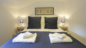 A bedroom with a large bed, two nightstands, two lamps, and a framed picture on the wall.