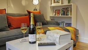 A living room with a sofa, a white coffee table with a bottle of wine, two glasses of wine, a remote control, and a book.