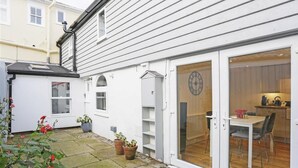 A white house with a tiled patio, a wooden dining area, and a clock on the door.