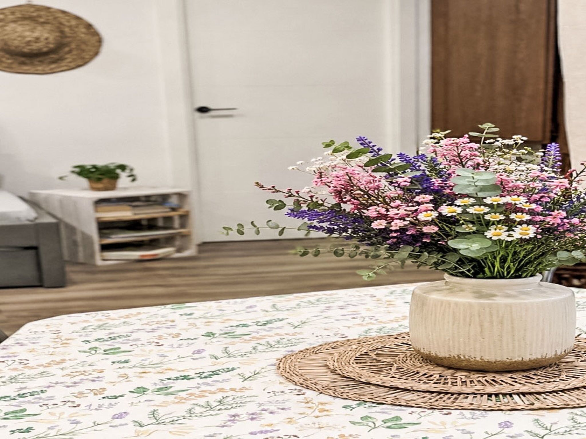 Une pièce avec une nappe à motifs floraux, un set de table en fibres tressées et un vase contenant un arrangement floral.