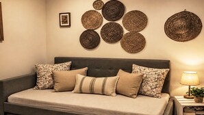 Ein gemütliches Schlafzimmer mit einer grauen Schlafcouch, gemusterten Kissen und einer Wand mit gewebten, runden Kunstobjekten.