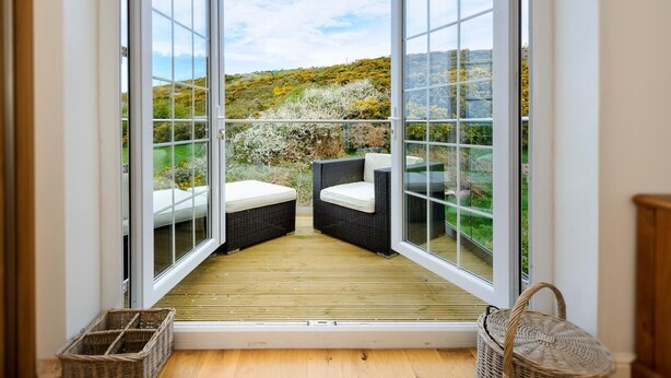 Un balcone con due divani in vimini e un pavimento in legno, affacciato su un giardino con alberi e arbusti.