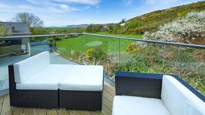Un balcone con mobili in vimini e una vista aperta su un paesaggio verde e delle colline.