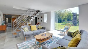 A modern living room with a grey sofa, a coffee table, and a staircase leading to an upper level. - 3 Bed in Botwnnog (oc-wag571) (Botwnnog)