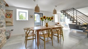 A spacious dining area with a wooden table and chairs, a vase with sunflowers, and a staircase leading to an upper level. - 3 Bed in Botwnnog (oc-wag571) (Botwnnog)