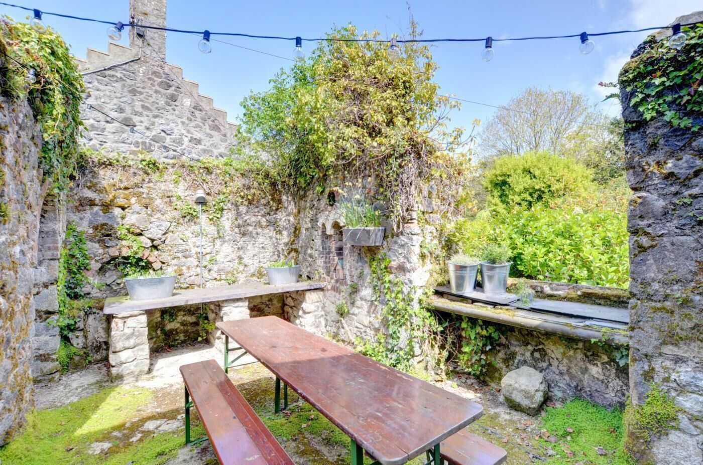 An outdoor patio area with stone walls, wooden benches, and potted plants.