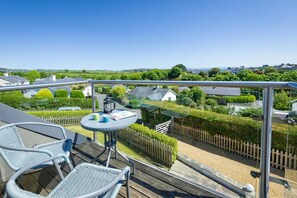A balcony with a table and chairs, overlooking a residential area with houses and greenery. - 4 Bed in Abersoch (oc-dolphb) (Abersoch)