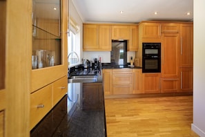 A modern kitchen with wooden cabinets, a stainless steel sink, and a black oven. - 4 Bed in Abersoch (oc-dolphb) (Abersoch)