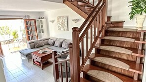 Una escalera con barandillas de madera que conduce a un piso superior, un sofá seccional gris, una mesa de centro de madera y una planta en maceta.
