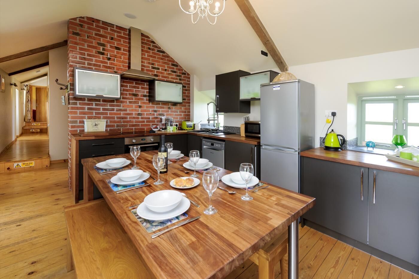 Una cocina moderna con pared de ladrillo, mesa de madera dispuesta para comer y horno empotrado.