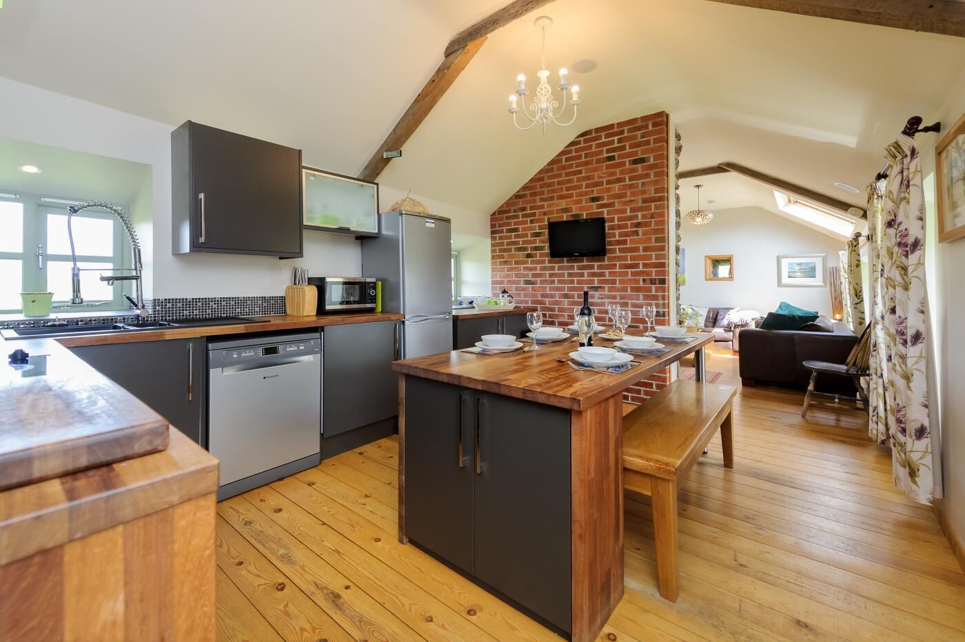 A kitchen with a wooden island, modern appliances, and a brick wall.
