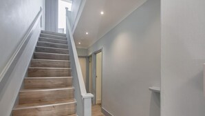 A staircase with wooden steps and white railings, leading to a room with a door and a light switch on the wall. - 2 Bed in Llanbedrog (oc-3glyny) (Llanbedrog)