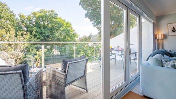 A balcony with wicker furniture, a dining table, and a sofa. - 2 Bed in Llanbedrog (oc-3glyny) (Llanbedrog)