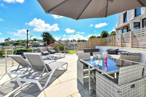 An outdoor patio with wicker furniture, a table with drinks, and a view of the sea and buildings in the background. - 2 Bed in Abersoch (oc-taflia) (Abersoch)