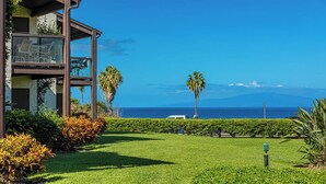 A hotel with a balcony overlooking a grassy area and the ocean.