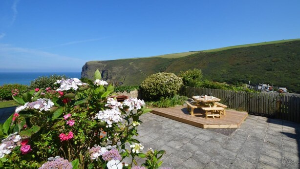 A patio with a wooden table and benches overlooking a coastal landscape with cliffs and greenery. - 2 Bed in Crackington Haven (oc-p00596) (Crackington Haven)