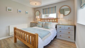 A bedroom with a wooden bed, two bedside tables, a window with curtains, and a radiator. - 2 Bed in Crackington Haven (oc-p00596) (Crackington Haven)