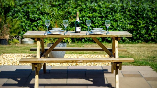 Juego de mesa de picnic de madera al aire libre con una botella y vasos.