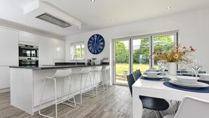 Una cucina moderna con mobili bianchi, una grande isola con sgabelli da bar e un'area da pranzo con tavolo per quattro persone.