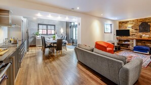 Eine moderne Küche mit Essbereich, ein Wohnzimmer mit Sofa und Fernseher sowie ein Kamin aus Stein.