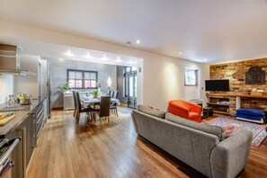 Eine moderne Küche mit Essbereich, ein Wohnzimmer mit Sofa und Fernseher sowie ein Kamin aus Stein.