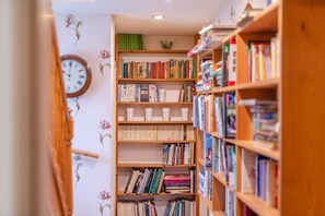 A narrow hallway with wooden bookshelves filled with books, a wall clock, and floral wallpaper. - 4 Bed in Helmsley (oc-y039) (Helmsley)