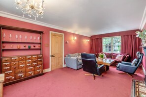 A room with a red carpet, a wooden cabinet with wine glasses, a sofa, a chair, and a table with a vase. - 4 Bed in Helmsley (oc-y039) (Helmsley)