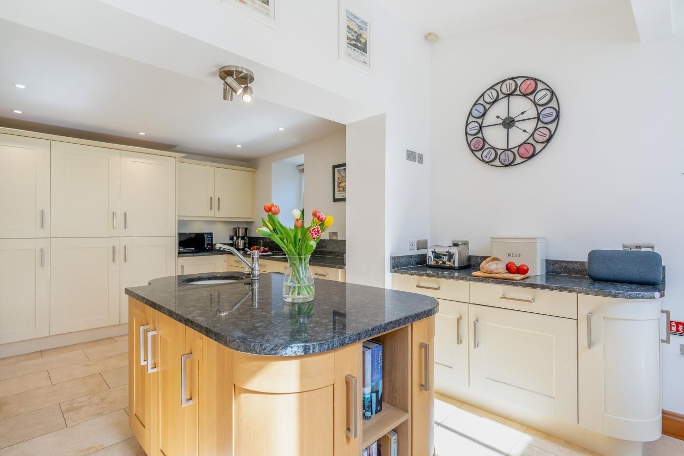 A modern kitchen with a central island, a wall clock, and a vase of tulips.