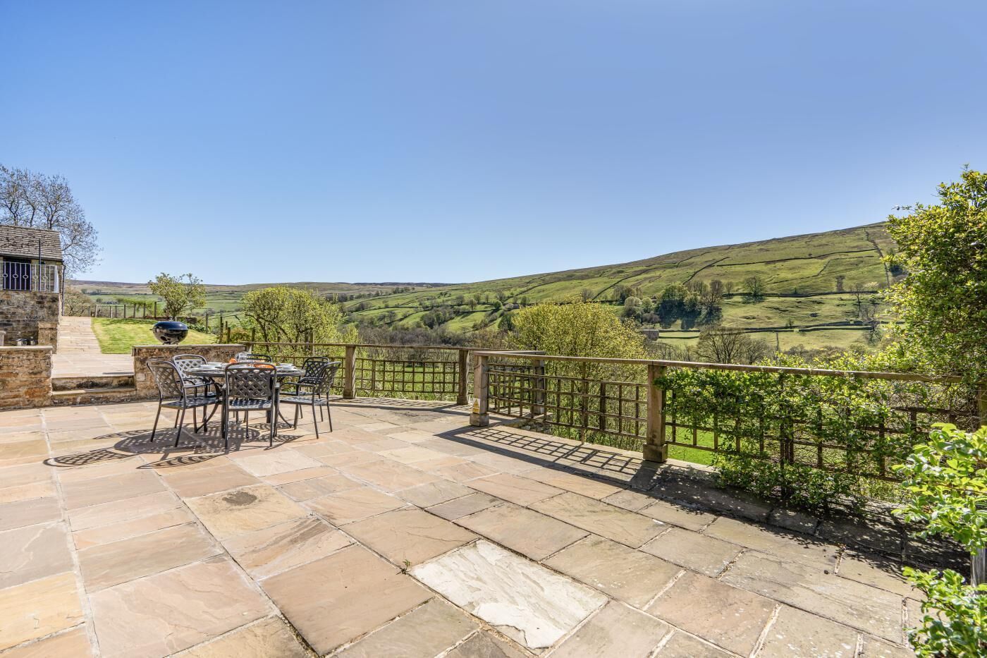 A patio with stone flooring, a table with chairs, and a view of rolling hills.