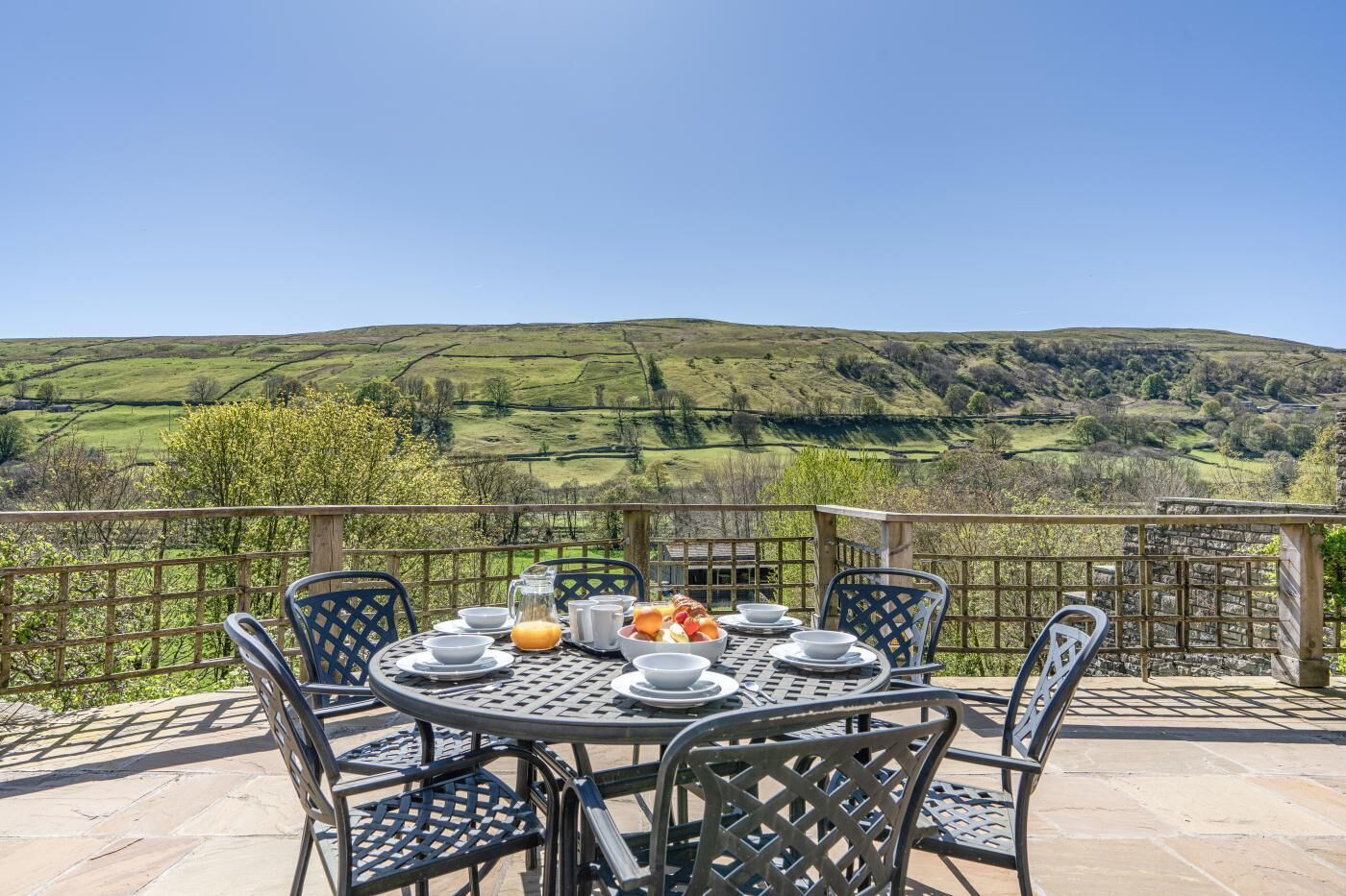A round table with chairs on a terrace with a view of rolling hills.