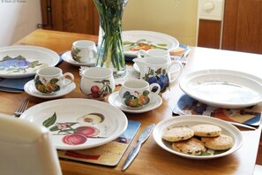 Ein Esstisch gedeckt mit Geschirr mit floralem Muster, Tassen und einer Vase mit grünen Stielen.