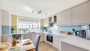 Une cuisine moderne avec un coin repas, dotée d’une grande fenêtre, d’appareils électroménagers en acier inoxydable et d’une table à manger en bois.